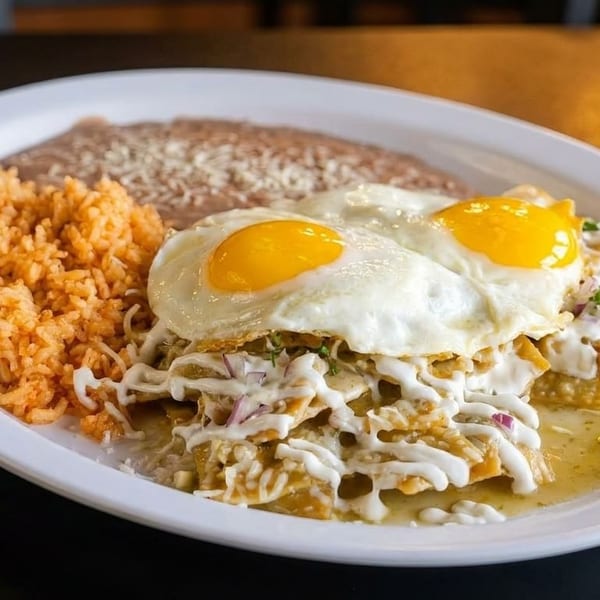 A plate of chilaquiles with two fried eggs, refried beans, and Spanish rice.