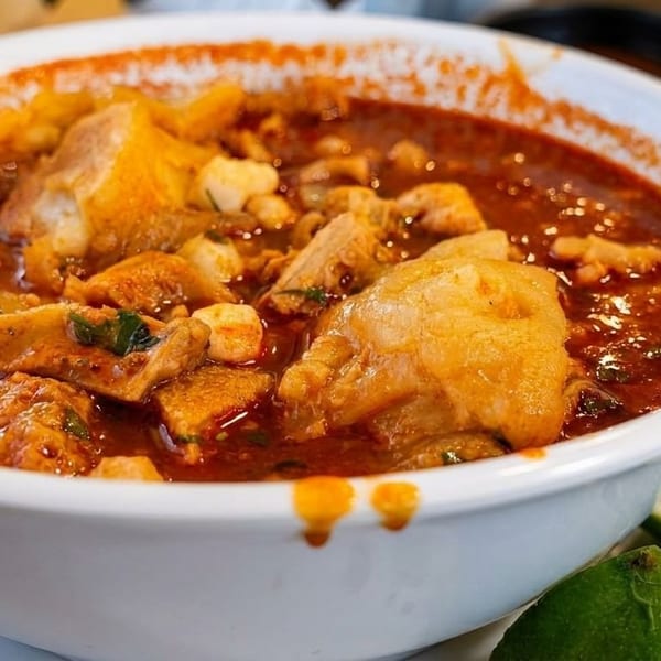 A white bowl filled with menudo, garnished with lime wedges and chopped cilantro.