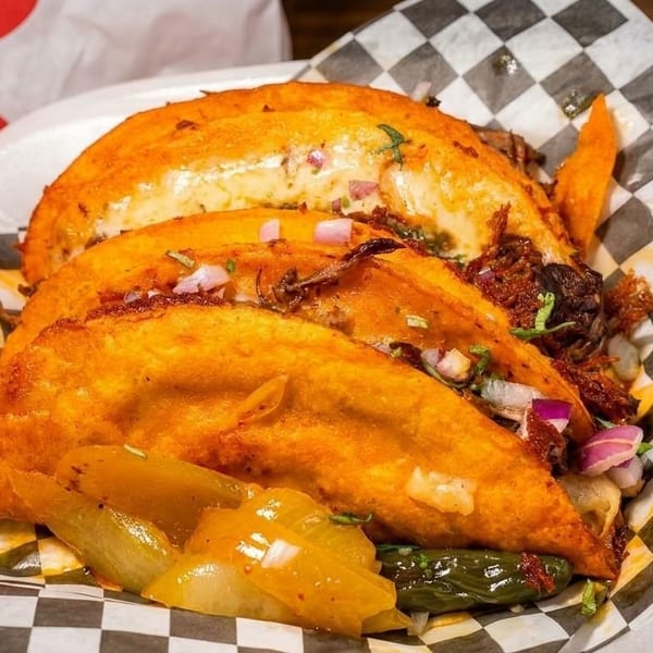 Three crispy birria tacos with red onions and cilantro, served with pickled peppers and onions.