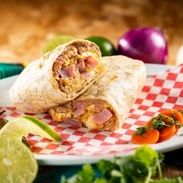 Two breakfast burritos with ham, egg, and cheese, served with lime, jalapeño, and carrots.
