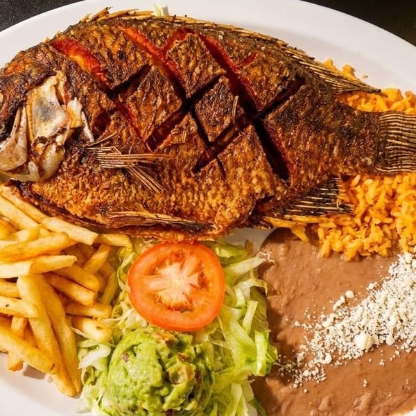 A whole fried fish with french fries, rice, refried beans, guacamole, and a tomato slice.